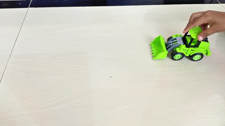 A small child is playing with a green construction truck toy. This toy resembles a bulldozer or wheel loader which is often used in construction work.