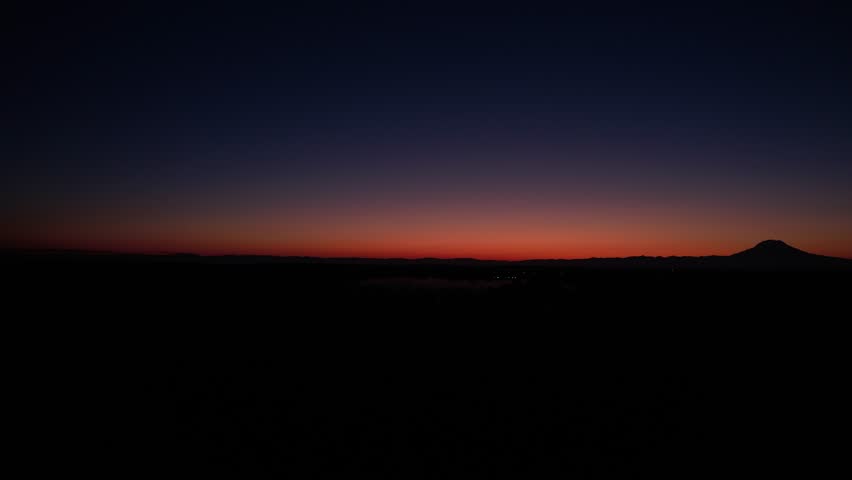 Pan drone shot of foggy sunrise over Mount Rainier (Tahoma) with forest and skyscape in Cascade Range, Mount Rainier National Park, west-central Washington state, USA