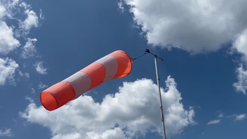 video of a wind sleeve to signal wind direction and intensity positioned at a parachute airfield, isolated against a blue sky with white clouds