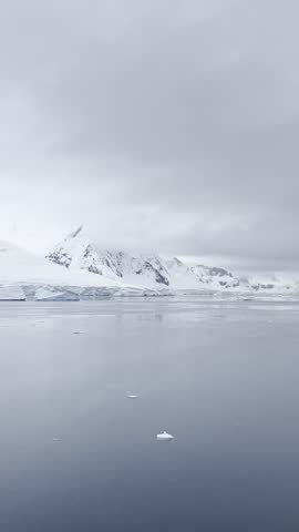 Polar seascape of Antarctica with icebergs floating in the ocean and glacier in the background. Antarctic land on a moody grey day. It exudes tranquility, with a pristine and untouched environment.