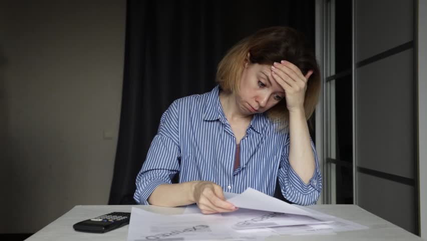 Stressed woman with debt utility bill, reading overdue electricity letter, struggling to pay