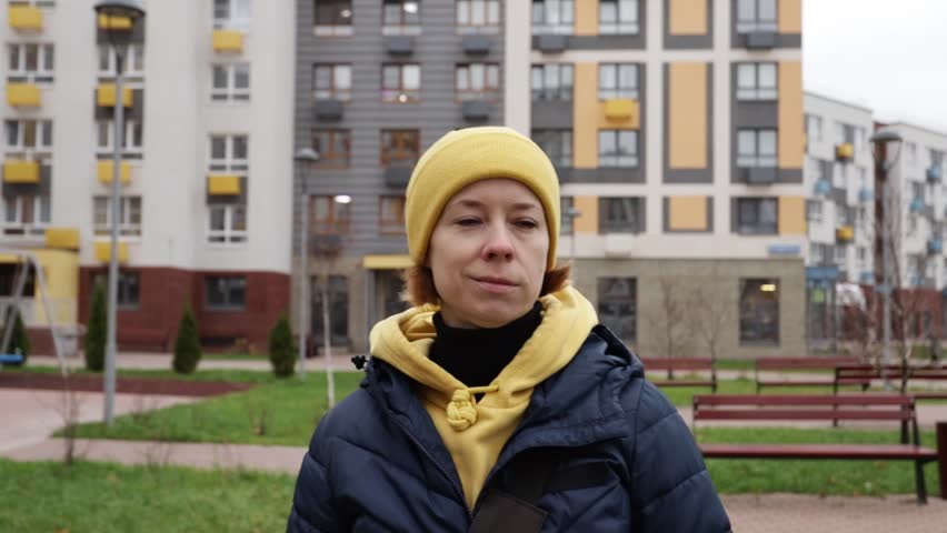A woman walks along a city street, outdoors in the modern cityscape, with her outfit reflecting the cool weather and season.