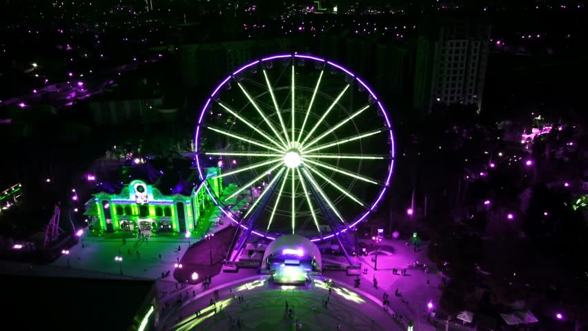 Aerial night neon illuminated Ferris wheel attraction in city amusement park