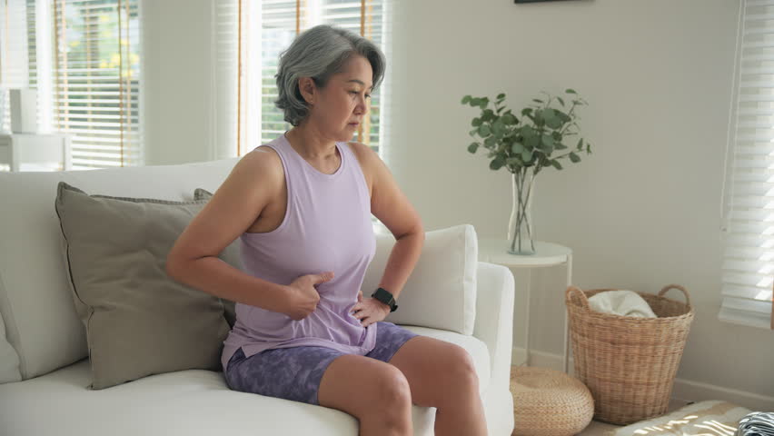 Asia adult middle age woman sit at sofa home feel pain elder gut health care aging system medical issue. Asian female old people Suffer stress cramp abdomen ache cancer illness menses period injury.