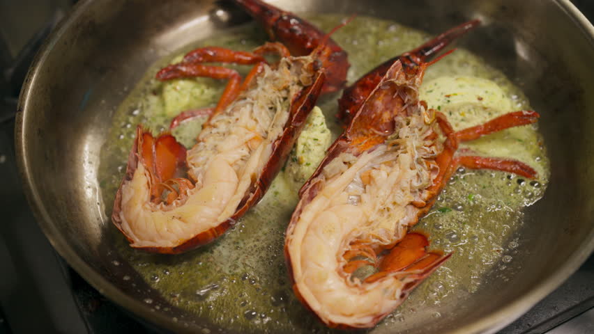 Two lobster halves cooking in butter in a pan.-closeup shot