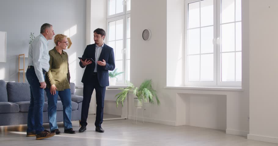 Happy elderly couple meets with a real estate agent or realtor, exploring a new home together. The clients review the property before deciding on a purchase or rental agreement or deal.