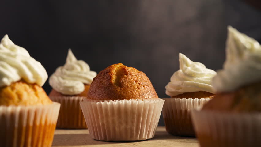 Freshly frosted cupcakes displayed on a tray ready to be served as piping tube descends and swirls, low angle static medium