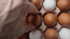 Human hand puts raw chicken egg in container. Box with rows of chicken fresh eggs. Carton filled with freshly collected brown eggs. Close-up in 4K, UHD - Powered by Shutterstock - Get 15% off with code: PIKWIZARD15