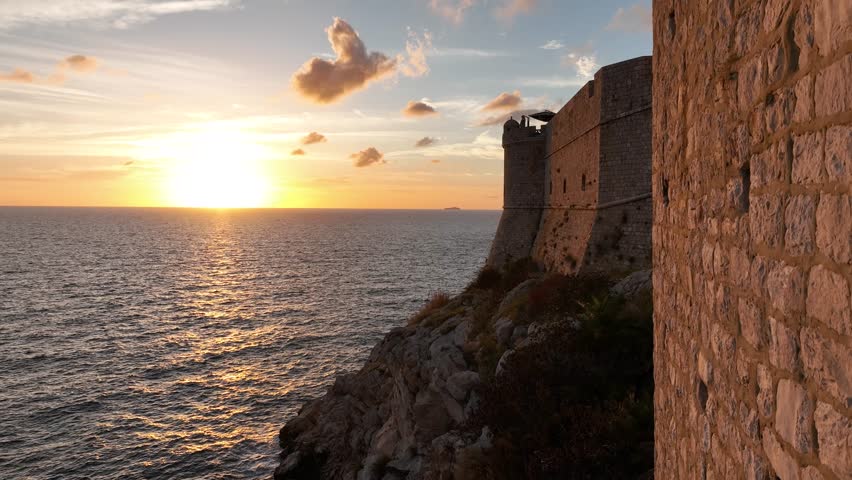 Aerial pedestal shot descending next to the city walls of Dubrovnik, Croatia looking out to the sun setting into the sea.
