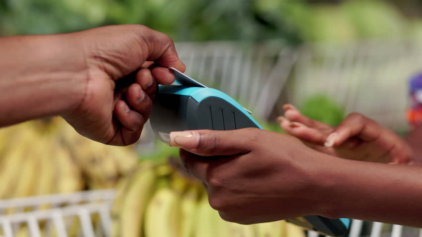 A customer makes contactless card payment via Point Of sale (POS) terminal, at fresh produce market where fruits and vegetables are sold.