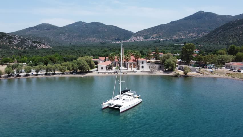 A luxury yacht sailing at seaport with Zaira hotel estate in view surrounded with olive trees garden and mountains, Mytilene, Lesvos Island, Establishing, Drone shot