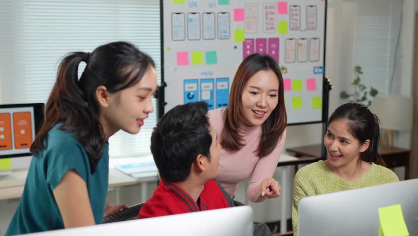 Diverse programming team collaborating on mobile app interface design, analyzing project details while working together at desktop computer in contemporary office environment