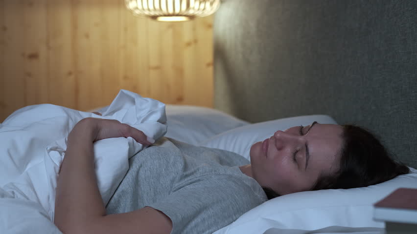 Woman sleeping peacefully, shifting positions in bed during restful night, experiencing deep relaxation within comfortable bedroom environment, embracing serene nighttime tranquility