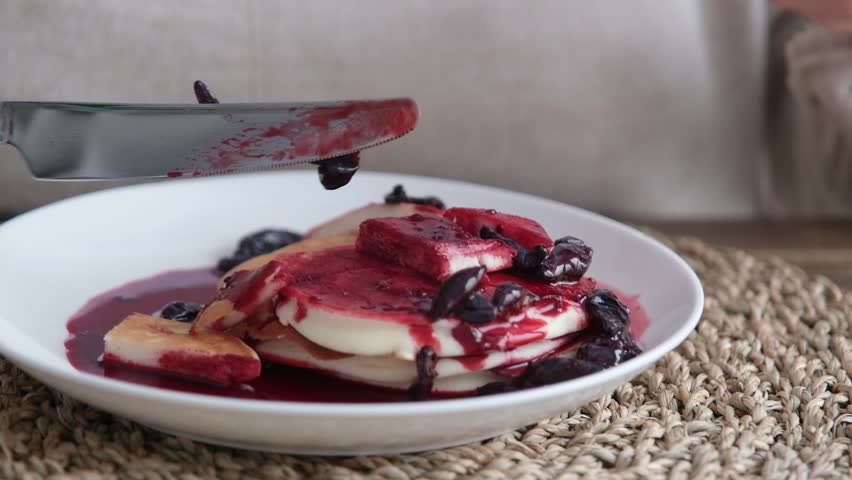 middle aged woman wearing home clothes eating pancakes with berry jam in the kitchen