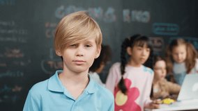 Smart boy looking at camera while diverse friend working or learning engineering code or prompt in STEM technology classroom. Cute student standing at camera while children using laptop. Erudition. - Powered by Shutterstock - Get 15% off with code: PIKWIZARD15