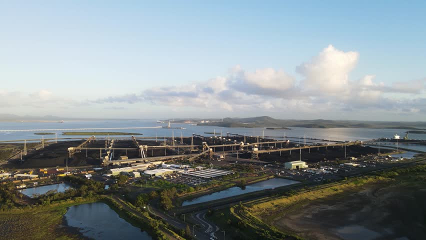 Contrasting scene of an industrial coal mining terminal against the backdrop of a tropical island view. Drone view