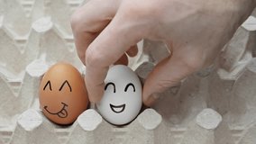 Human hand puts raw chicken eggs with happy faces in container. Box with rows of chicken fresh eggs. Smiling, sad, angry faces. Happy easter. Close-up in 4K, UHD - Powered by Shutterstock - Get 15% off with code: PIKWIZARD15