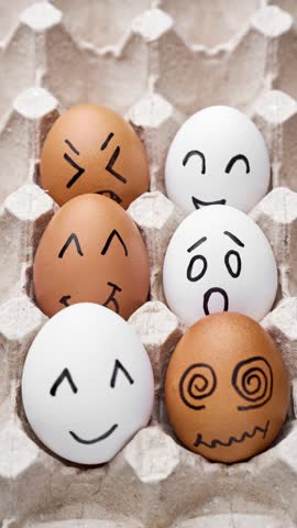 Eggs with funny faces in box. Happy, angry, sad, surprised faces on white and brown eggs. Vertical video. Stop motion. Funny cartoon faces. Food concept. Close-up of hen eggs. 4K, UHD