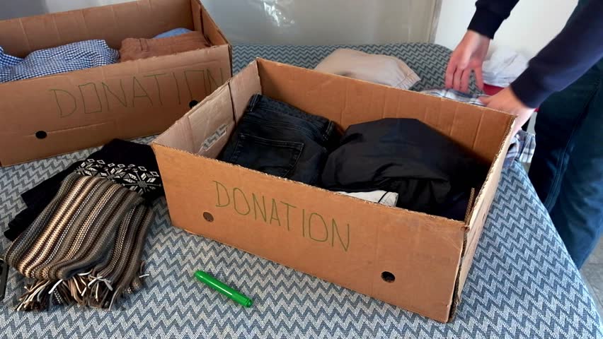 Sorting clothes for donations. Cardboard donation box with things. Help for poor and needy people.
