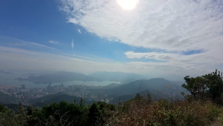 A timelapse of a view overlooking Zhuhai, China from the hills above, with a clear sky, white clouds, and greenery in the foreground