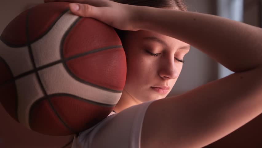 Young female basketball player holding ball on shoulder