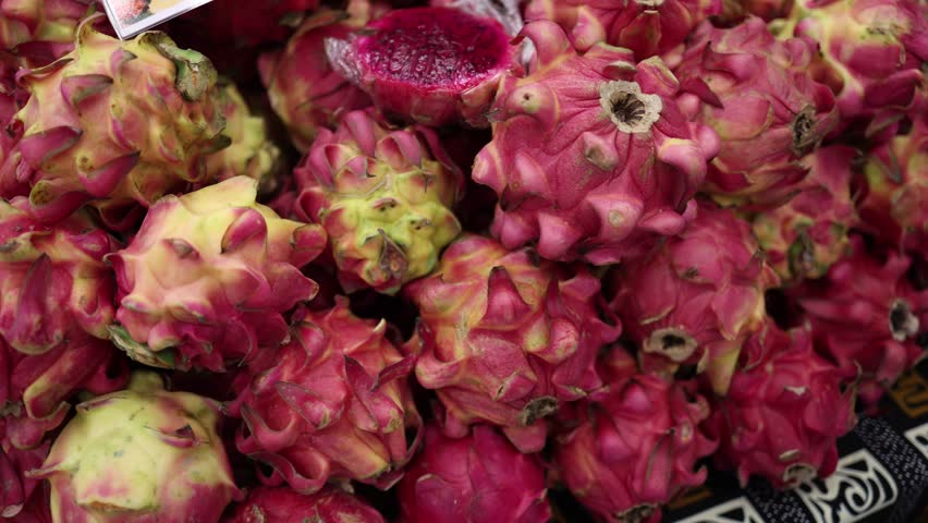 A close-up video of dragon fruits with one sliced open, revealing the bright pink pulp inside. The camera captures the vibrant colors and unique texture of these exotic fruits.