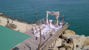 A beautiful wedding setup is prepared on a wooden pier overlooking the calm ocean waters. The elegant decor features floral arrangements and white seating, creating a romantic ambiance. - Powered by Shutterstock - Get 15% off with code: PIKWIZARD15