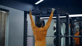 Crossfit athlete doing pull-ups at the gym - rear view. Handsome man in orange sportwear doing functional training on horizontal bar - slow motion - Powered by Shutterstock - Get 15% off with code: PIKWIZARD15