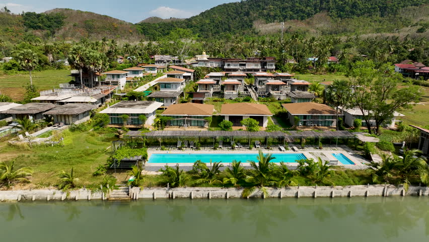 Tropical beachfront villas overlooking a turquoise bay surrounded by lush green hills and calm sea waters. Koh Yao Yai, Thailand.