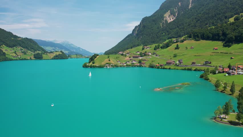 Drone footage of turquoise clear lake Lungern or Lungerersee in Switzerland in summer sunny day with village and green meadow