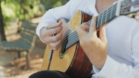 Professional guitarist plays guitar outdoors. Musician plays a classical guitar in the park. A man in a white shirt plays a musical instrument outside the house. The guitarist plays the guitar. - Powered by Shutterstock - Get 15% off with code: PIKWIZARD15