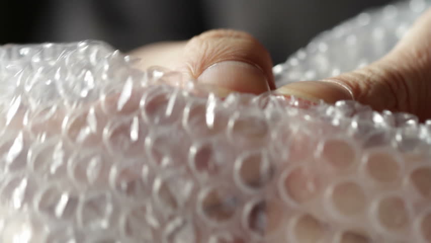 Fingers bursting air pockets in a sheet of transparent bubble wrap. Recorded
