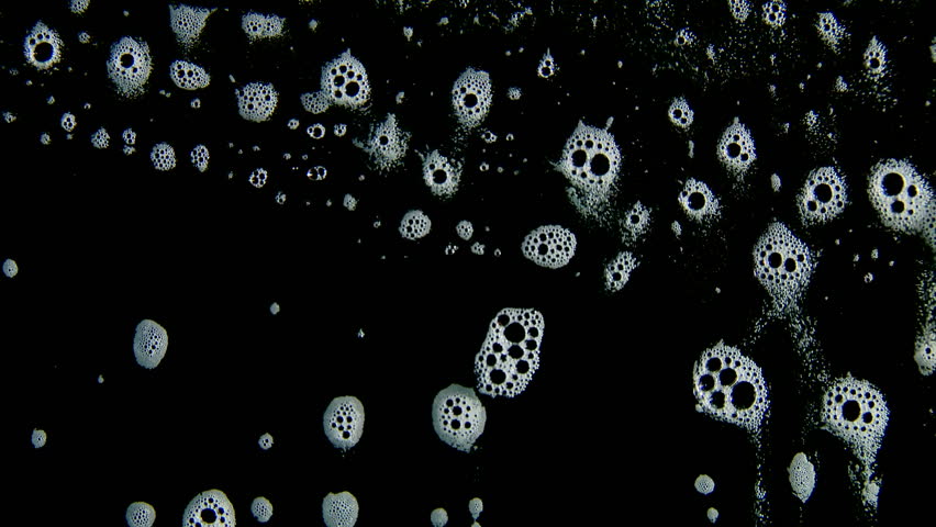 White foam bubbles running through liquid downwards against a black background.
