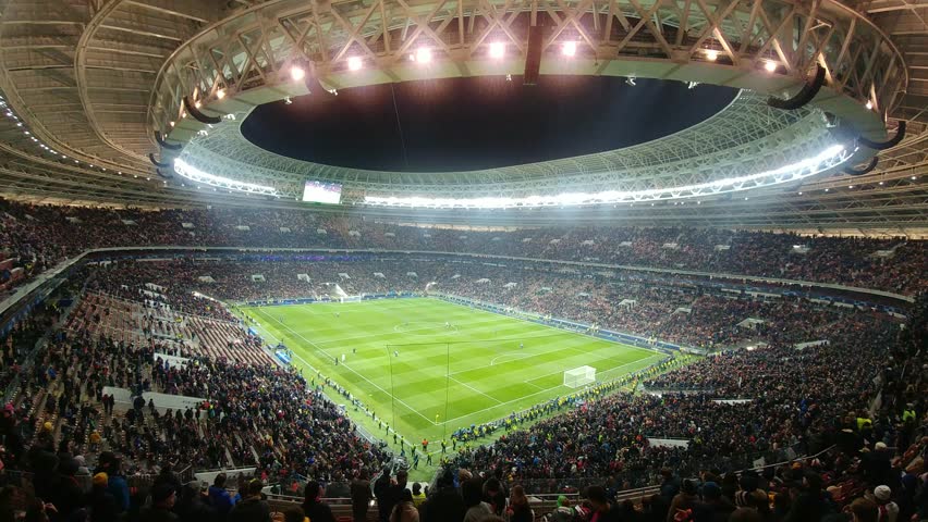 Stadium full of people watching a soccer game. The field is green and the stands are packed