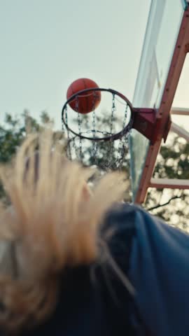 A focused blonde girl dribbles a basketball and throws it into the hoop while playing basketball on a street court