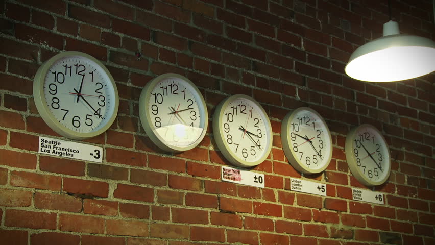 Set of five clocks showing different timezones on an interior brick wall with an