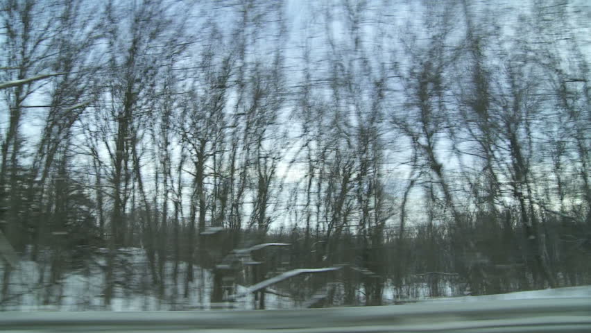 View from car window while driving past snow-covered slopes, trees and under