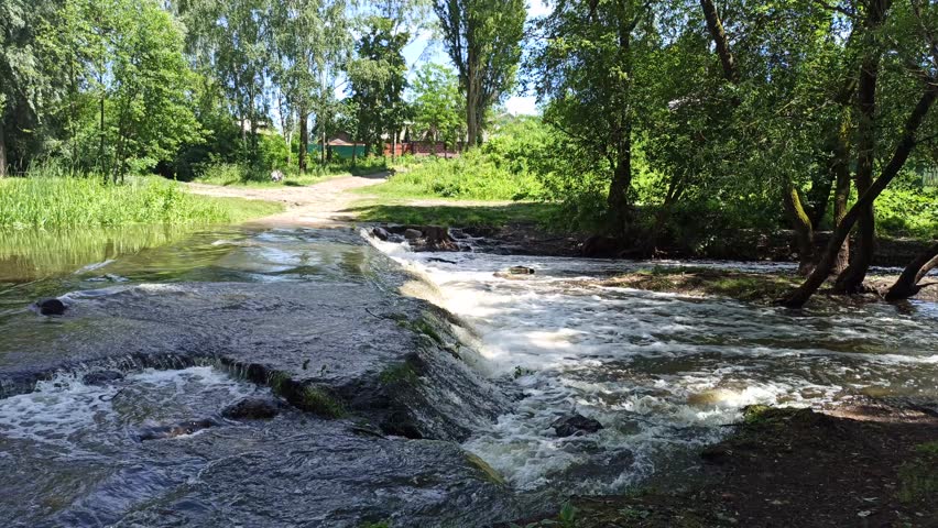 Small waterfalls among the stones and vegetation in Chernihiv. Pavlovskyi waterfall in Chernihiv. Small beautiful waterfall in a green forest
