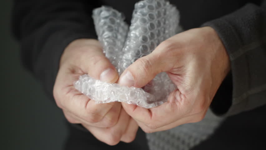 Hands bursting air pockets in a sheet of transparent bubble wrap. Macro shot