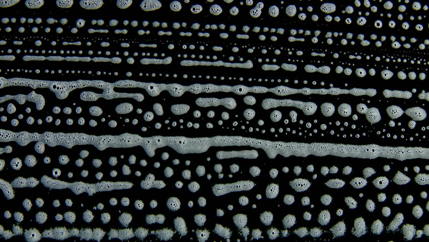 Lines of white foam bubbles slowly running downwards against a black background.