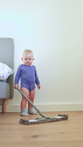 Little boy toddler washes the floor with a mop. Child helps clean the floor. Boy in a cotton bodysuit.
