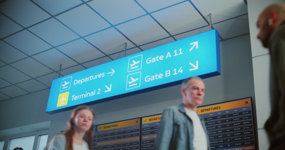 Crowd of Diverse People Walking in Modern International Airport Terminal. Illuminated LED Sign Directing Passengers to Departures and Gates for Boarding Flight, Digital Arrival and Departure Screen.