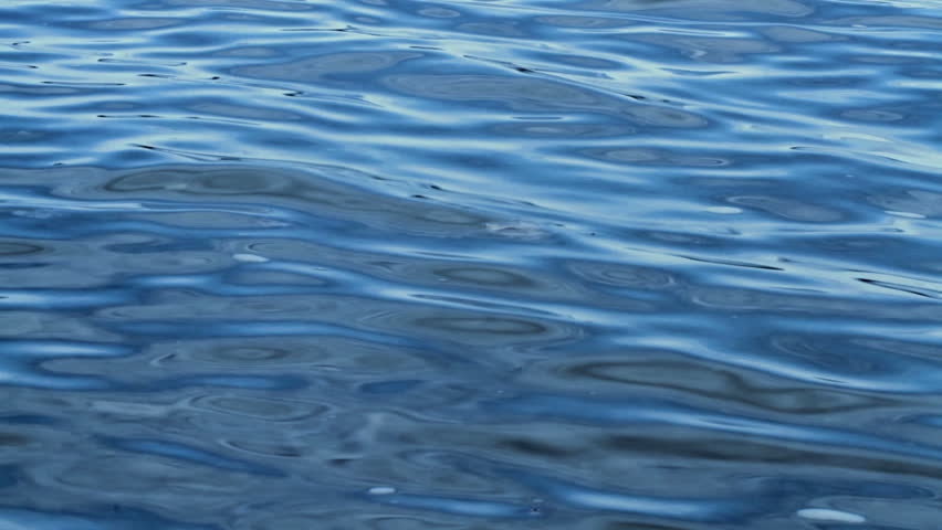 Blue waves flow towards a lake or sea shore. Looping clip.