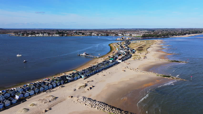 Reversing aerial shot over Mudeford Sandbar with beach huts on sunny day