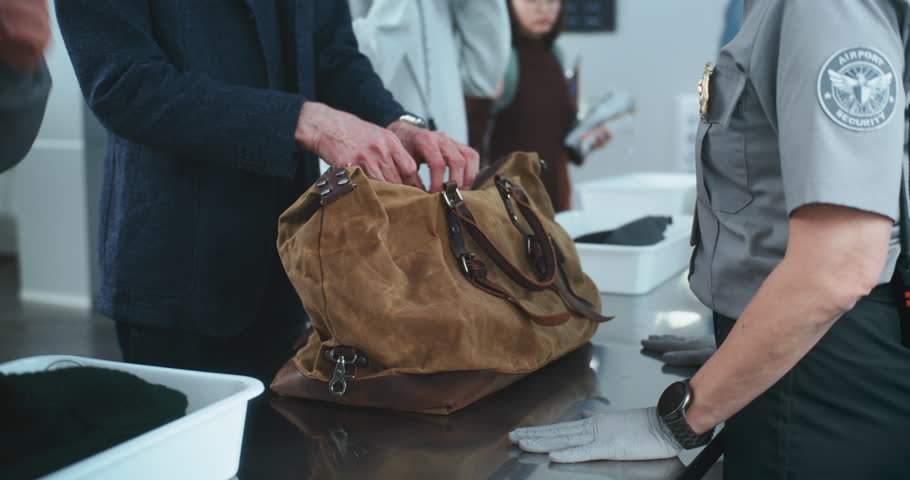 Security Checkpoint in International Airport: Close Up of Security Officer Checking Bag of Tourist for X-ray Scanning before Boarding Flight. Queue of Diverse People During TSA Screening Procedures.