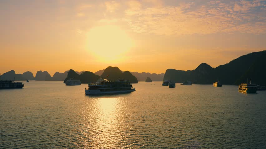 Many Cruise ships anchored at Halong Bay back lit with rising sun, Vietnam