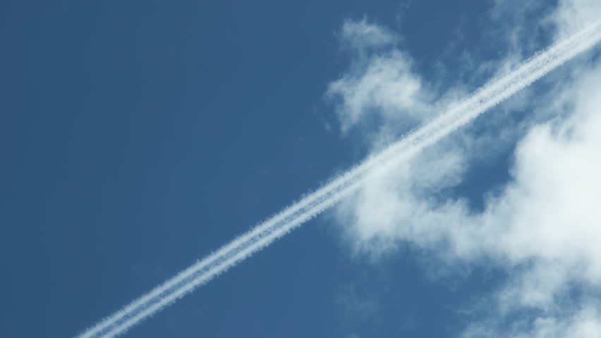 Condensation trails left by a plane in a blue sky with white clouds. Slow motion.