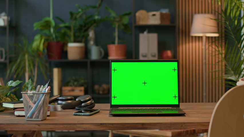 Pan shot of wireless laptop with green chroma key screen at desk in workspace with plants in background, no people
