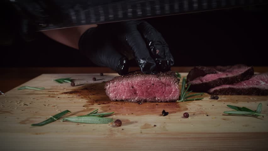Chef slicing juicy tenderloin steak with a knife on a wooden cutting board in the kitchen, slow motion, close up
