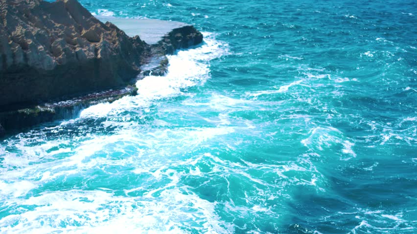Turquoise blue ocean waves crash against rocky shoreline off coast of Puerto Rico